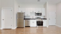 Located at 307 E 1st St in Dayton, Ohio, this single-floor unit presents a clean, modern aesthetic throughout its well-appointed interior. The space features warm wood-look laminate flooring that runs continuously throughout, lending a cohesive and polished look to every room.

The kitchen is a standout feature, designed with functionality and style in mind. White shaker-style cabinetry with matte black hardware reaches toward the ceiling, maximizing storage capacity. Dark quartz countertops provide a striking contrast against the white cabinetry, while a full suite of stainless steel appliances—including a refrigerator, electric range, built-in microwave, and dishwasher—offers modern convenience. A single-basin undermount sink with a contemporary pull-down faucet completes the kitchen setup.

The living area is open and airy, benefiting from tall ceilings and natural light admitted through a large window fitted with horizontal blinds. The neutral wall tones and clean lines contribute to a calm, versatile atmosphere easily adaptable to various furnishing styles.

The bathroom maintains the same modern design language, featuring a white vanity with dark countertop, matte black hardware, and a wall-mounted mirror, all set against the same wood-look flooring found throughout the unit. The overall ambiance is fresh, contemporary, and move-in ready.