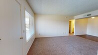 This single-floor unit at 6161 E Grant Rd in Tucson, Arizona offers a functional and straightforward layout designed for comfortable everyday living. The living area is generously sized, featuring neutral-toned carpet, soft natural light from a large window with blinds, and a textured ceiling throughout. An open sightline connects the living space to the kitchen, creating an easy flow between the two areas.

The galley-style kitchen is efficiently laid out, featuring warm wood-toned upper cabinetry, a white electric range, a refrigerator, and wood-look flooring that adds a touch of warmth. A separate door in the kitchen provides additional access or storage convenience.

The bedrooms are carpeted and well-proportioned, each benefiting from natural light via windows. The primary bedroom includes a closet and direct access to a bathroom, while additional bedrooms feature their own closet spaces. The bathrooms are practical and clean, with one offering a vanity with under-sink cabinetry, a large mirror, and a shower-tub combination, and another featuring a wide vanity counter with ample storage beneath. Wood-look flooring carries through the bathroom spaces, complementing the overall aesthetic. The unit's neutral color palette and consistent finishes create a cohesive, move-in-ready environment.