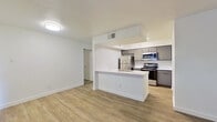 This single-floor unit offers a thoughtfully designed layout with a modern, clean aesthetic. The open-concept living and kitchen area is anchored by warm wood-look luxury vinyl plank flooring that flows seamlessly throughout the main living spaces. The kitchen is a standout feature, equipped with stainless steel appliances including a refrigerator, electric range, and over-the-range microwave, all complemented by sleek gray cabinetry, white subway tile backsplash, and light countertops. A peninsula with an integrated sink provides additional workspace and casual dining potential, connecting the kitchen to the main living area. The living room is bright and inviting, featuring a tile-surround fireplace with a warm wood mantel as its focal point, flanked by windows fitted with horizontal blinds that allow for natural light control. The bedroom is carpeted for comfort and includes dual doors, offering access to a closet and an adjoining room. The bathroom is clean and functional, featuring a full tub and shower combination with white tile surround, a toilet, and gray vanity cabinetry. A dedicated entry area with wood-look flooring provides a practical transition into the living space. Overall, the unit presents a cohesive, updated interior ready for comfortable living.