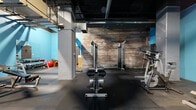 Located at 1900 E Superior Ave in Cleveland, Ohio, this fitness facility offers a generously sized, open-plan workout space that blends industrial character with functional design. The space is defined by its striking architectural details, including exposed brick walls, dark open-ceiling ductwork, and concrete support columns that lend a raw, urban aesthetic. Vivid blue accent walls provide a bold contrast against the darker structural elements overhead, creating an energetic and motivating atmosphere.

The rubber-tiled floor spans the full footprint of the space, providing durable, impact-absorbing coverage suitable for a wide range of workout activities. The facility is well-equipped with a comprehensive selection of fitness equipment, including treadmills, elliptical machines, stationary bikes, a stair climber, cable and weight machines, a squat/power rack, adjustable benches, a dumbbell rack with a full set of free weights, and a stability ball. The layout is organized to allow ample circulation between equipment zones.

A mirrored section along one wall supports strength training and form monitoring, while a small enclosed room—likely a sauna or private utility space—is visible toward the rear of the facility. Industrial pendant and recessed lighting illuminate the space throughout. The overall ambiance is functional and focused, catering to a full-body training experience within a distinctly urban Cleveland setting.