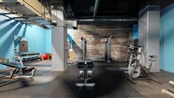 Located at 1900 E Superior Ave in Cleveland, Ohio, this fitness facility offers a generously sized, open-plan workout space that blends industrial character with functional design. The space is defined by its striking architectural details, including exposed brick walls, dark open-ceiling ductwork, and concrete support columns that lend a raw, urban aesthetic. Vivid blue accent walls provide a bold contrast against the darker structural elements overhead, creating an energetic and motivating atmosphere.

The rubber-tiled floor spans the full footprint of the space, providing durable, impact-absorbing coverage suitable for a wide range of workout activities. The facility is well-equipped with a comprehensive selection of fitness equipment, including treadmills, elliptical machines, stationary bikes, a stair climber, cable and weight machines, a squat/power rack, adjustable benches, a dumbbell rack with a full set of free weights, and a stability ball. The layout is organized to allow ample circulation between equipment zones.

A mirrored section along one wall supports strength training and form monitoring, while a small enclosed room—likely a sauna or private utility space—is visible toward the rear of the facility. Industrial pendant and recessed lighting illuminate the space throughout. The overall ambiance is functional and focused, catering to a full-body training experience within a distinctly urban Cleveland setting.