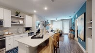 This thoughtfully designed single-floor residence combines contemporary style with functional living. The open-concept layout connects the kitchen, dining, and living areas seamlessly, creating an inviting and spacious flow. The kitchen is outfitted with crisp white cabinetry, stainless steel appliances including a refrigerator, range, and microwave, a subway tile backsplash, and a generous island with bar seating — ideal for casual dining or entertaining. Wood-look flooring runs throughout the main living areas, adding warmth and continuity. The living room features large windows and a glass door that flood the space with natural light, complemented by a ceiling fan and a bold teal accent wall that adds a vibrant focal point. Two well-proportioned bedrooms offer plush carpeting, ceiling fans, and ample natural light from large windows dressed with sheer curtains. Each bedroom features its own distinct design, with soft accent walls and generous space for furnishings. The unit includes two full bathrooms: one with a soaking tub and tile surround, and another with a walk-in glass-enclosed shower, both finished with wood-look flooring, white vanities, and recessed lighting. The overall ambiance is modern, clean, and comfortable throughout.