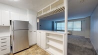 Located at 910 Pennsylvania Ave in Kansas City, MO, this two-bedroom residence offers a practical and well-organized single-floor layout. The kitchen is outfitted with clean white cabinetry extending to the ceiling for ample storage, a stainless steel refrigerator, and tile flooring. A built-in pass-through with open shelving connects the kitchen to the living area, creating an open, communicative flow between spaces. The living area features neutral carpet, wide windows with horizontal blinds that invite natural light, and a wall-mounted HVAC unit. The primary bedroom is a generously sized retreat with plush carpeting, multiple louvered bi-fold closet doors providing substantial storage, and a window for natural light. The second bedroom is a comfortable, carpeted room with soft blue-gray walls and ample space. Both bedrooms offer a quiet, functional atmosphere. Throughout the residence, a consistent neutral color palette of whites and soft grays creates a cohesive and understated aesthetic. The layout is efficient, making practical use of every area within the space.
