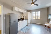This 260 square foot studio apartment, located at 5667 Santa Monica Blvd in Los Angeles, offers a thoughtfully designed living space. The single-floor layout comprises a main living area, a kitchen, a bathroom, and a closet. The living area features neutral-toned walls and wood-look flooring, creating a bright and open atmosphere. A contemporary white armchair and footstool, accompanied by a sleek floor lamp, provide a cozy seating nook.

The kitchen is a highlight of the space, boasting modern white cabinetry with ample storage both above and below the countertops. Stainless steel appliances, including a full-sized refrigerator, blend seamlessly with the design. The dark countertops contrast nicely with the white cabinets, and a window allows natural light to flow in. A blue patterned rug adds a pop of color to the kitchen floor.

The bathroom, while compact, is efficiently designed with a white pedestal sink, toilet, and what appears to be a shower or bathtub area. A framed mirror and towel ring contribute to the functionality of the space. The apartment's closet, though not visible in the images, adds valuable storage to this well-planned studio. Overall, this apartment maximizes its limited square footage through smart design choices and a cohesive, modern aesthetic.