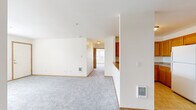 Located in Salem, Oregon, this one-bedroom, two-bathroom residence offers a well-organized single-floor layout designed for comfortable everyday living. The open living room is generously proportioned, featuring soft gray carpeting, neutral cream walls, warm wood trim, and a ceiling fan overhead. Large windows fitted with blinds invite natural light and provide views of the surrounding neighborhood. The kitchen is efficiently arranged in an L-shaped configuration, featuring warm oak cabinetry, tile flooring, a full suite of white appliances including a refrigerator, range, microwave, and dishwasher, and a peninsula with a built-in sink that opens toward the living area — ideal for casual dining or entertaining. The bedroom is a comfortable, carpeted retreat with windows overlooking greenery and easy access to the bathrooms. Both bathrooms are finished with tile flooring, oak vanity cabinetry, countertop sinks, and large mirrors. The primary bathroom includes a shower-tub combination with safety bars, while the second bathroom features a similar vanity setup. Consistent warm wood-toned finishes, neutral walls, and practical flooring choices give the space a cohesive and functional character throughout.