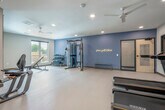Located at 3900 Monona Dr in Madison, Wisconsin, this fitness center offers a thoughtfully designed, single-floor layout divided into two functional workout areas. The space features a clean, modern aesthetic with neutral-toned walls, durable light-colored flooring, and recessed lighting throughout, creating a bright and welcoming environment. Ceiling fans provide additional airflow across both rooms.

The main workout area is generously sized, housing a variety of cardio and strength equipment including treadmills, an elliptical, a rowing machine, a stationary bike, a cable machine, an adjustable weight bench, and a dumbbell rack. Floor-to-ceiling mirrors line the walls, enhancing the sense of openness and allowing users to monitor their form. Natural light filters in through several windows, adding to the energetic atmosphere. A motivational neon sign accents one of the accent walls, painted in a calming blue-grey tone.

The second room functions as a dedicated studio or group fitness space, also lined with large mirrors and featuring a wall-mounted television for guided workouts. Wall-mounted storage racks keep fitness accessories such as resistance bands, yoga rings, and step platforms neatly organized. The studio's open floor plan makes it ideal for stretching, yoga, or aerobic sessions. A rowing machine and additional small equipment round out this versatile space. Together, the two areas offer a comprehensive and well-appointed fitness facility.