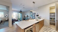 Located in the heart of Old Town Scottsdale at 6901 E Main St, this well-appointed 2-bedroom, 2-bathroom residence offers a thoughtfully designed open-concept layout with modern finishes throughout. Light wood-tone flooring runs seamlessly across the single-floor plan, complementing the clean, neutral palette.

The kitchen serves as the centerpiece of the living space, featuring a large quartz-topped island with seating for three, warm wood cabinetry, a tile backsplash, and a full suite of stainless steel appliances including a gas range, microwave, refrigerator, and dishwasher. A dedicated pantry closet adds convenient storage. Pendant lighting above the island and a linear overhead fixture complete the contemporary aesthetic.

The living room opens directly to a private balcony through floor-to-ceiling sliding glass doors, filling the space with natural light and providing outdoor views of the Scottsdale surroundings. The primary bedroom is generously sized, offering a serene retreat with a walk-in closet and an en-suite bathroom appointed with large-format stone tile, a glass-enclosed walk-in shower, wood vanity with quartz countertop, and a wide vanity mirror. The second bedroom is equally well-finished, with wall sconces and ample closet space. Three total closets ensure abundant storage throughout the residence.