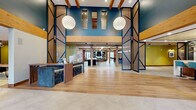 Located at 4066 Lexington Ave N in Shoreview, Minnesota, this expansive single-floor amenity space makes a striking first impression with a soaring double-height entry lobby. Exposed wood beams, bold teal accent walls, decorative lattice panels framed in black steel, and large globe pendant lights establish a modern yet warm architectural character throughout. Wide-plank hardwood and large-format tile flooring guide visitors seamlessly from zone to zone.

The reception area features a custom stone-and-wood front desk, flanked by floor-to-ceiling glass walls that flood the entrance with natural light and views of the outdoors. Beyond the lobby, an open lounge and dining area offers a mix of seating, including leather sofas, café-style tables, and a statement fireplace, all beneath vaulted wood-beam ceilings.

A dedicated co-working zone provides communal long tables and task seating against a bold graphic-striped accent wall. A formal conference room is equipped with a solid wood table, upholstered chairs, pendant lighting, and a wall-mounted display screen. The theater room delivers a premium experience with rows of quilted leather recliner seating and a ceiling-mounted projector. Additional private rooms, a full kitchen, and carpeted breakout nooks round out this richly detailed, multi-functional community space.