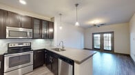 Located at 21525 Spring Plaza Dr in Spring, TX, this one-bedroom, one-bathroom residence offers a thoughtfully designed single-floor layout with modern finishes throughout. The open-concept kitchen and living area serves as the heart of the home, anchored by a large peninsula with quartz countertops, an undermount sink, and elegant pendant lighting. Dark espresso cabinetry—including glass-front upper cabinets—contrasts beautifully with a marble-style tile backsplash, while a full suite of stainless steel appliances, including a French door refrigerator, electric range, built-in microwave, and dishwasher, provides a complete culinary experience. The living area features light wood-tone flooring and a ceiling fan, with French doors that invite natural light and provide outdoor access. The bedroom is carpeted for comfort, includes a ceiling fan, and features a window with outdoor views. Two closets offer generous storage. The bathroom is finished with large-format tile surrounding a soaking tub and shower combination, complemented by neutral tile flooring. A dedicated laundry area adds everyday convenience. The space presents a clean, contemporary aesthetic with a neutral color palette throughout.