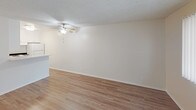 This single-floor residence offers a straightforward, functional layout designed for comfortable everyday living. The main living area is highlighted by durable wood-style laminate flooring, neutral beige walls, and a textured ceiling equipped with a ceiling fan and light fixture. A large window with vertical blinds allows natural light to fill the space, creating a bright and airy atmosphere. Adjacent to the living area, the layout opens toward the kitchen, which features white cabinetry with brushed nickel hardware, speckled laminate countertops, a stainless steel double-basin sink, and a gas range — providing a practical and clean cooking environment. A pass-through counter connects the kitchen to the living space, enhancing the open feel of the floor plan. The bedroom is carpeted in warm neutral tones, offering a quieter, softer underfoot experience, and includes a window with vertical blinds for natural light and privacy. The bathroom is efficiently designed, featuring a speckled laminate vanity countertop with white cabinetry, a standard toilet, a wall-mounted towel bar, and a shower-tub combination. Wood-style flooring continues into the bathroom, maintaining a cohesive aesthetic. Overall, the space presents a clean, move-in ready environment with consistent neutral tones throughout.