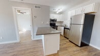 Located at 13301 Plaza Terr in Oklahoma City, OK, this single-floor residence offers a clean, modern aesthetic accented by warm wood-look flooring and neutral gray walls that flow consistently throughout the space. The open-concept layout connects the kitchen and living areas seamlessly, creating a functional and inviting atmosphere.

The kitchen is a standout feature, equipped with a full suite of stainless steel appliances, including a refrigerator, range, over-the-range microwave, and dishwasher. White shaker-style cabinetry with brushed hardware lines the walls, complemented by a classic white subway tile backsplash and gray quartz-style countertops. A peninsula island provides additional prep space and casual seating potential, enhancing the kitchen's practicality.

The living and entry areas are open and bright, benefiting from large sliding glass doors dressed with vertical blinds that allow generous natural light to filter in. Recessed lighting and a ceiling fan further illuminate the space. The bathroom includes a soaking tub and features a gold-toned grab bar, adding a subtle warm accent. Throughout, the space maintains a cohesive, contemporary feel with clean lines and a neutral palette well-suited for a variety of interior styles.