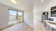 This contemporary single-floor unit at 3725 N 27th St in Tacoma, Washington offers a clean, modern aesthetic defined by crisp white walls, light hardwood-style flooring, and an abundance of natural light. The open-concept living and dining area is anchored by oversized windows that frame pleasant neighborhood and treetop views, filling the space with warmth throughout the day. Recessed lighting complements the natural light, ensuring a well-lit environment at all hours.

The kitchen is thoughtfully designed with flat-front gray cabinetry, stainless steel appliances including a refrigerator, electric range, microwave, and dishwasher, as well as light countertops and a functional layout that makes excellent use of the available space. It flows seamlessly into the living area, creating an inviting open atmosphere.

The bedroom is well-proportioned and bright, featuring a large window that continues the natural light theme and overlooks a landscaped exterior. A sliding door leads to a closet, adding practical storage. The bathroom maintains the unit's clean, modern character with a wide vanity, undermount sink, white countertop, full-width mirror, and light cabinetry. Light flooring ties the spaces together cohesively throughout the entire unit.