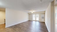 This 670 square foot apartment in Gastonia, NC offers a well-designed living space on a single floor. The layout comprises a combined kitchen and living room, one bedroom, one bathroom, and a closet. The kitchen is equipped with modern appliances, including a black refrigerator and electric stove, complemented by ample wooden cabinetry and light-colored countertops. The living area is spacious, featuring wood-look laminate flooring and a ceiling fan for comfort. Large French doors in this area provide natural light and access to an outdoor space. The bedroom, measuring 140 square feet, includes a window and is fitted with plush carpeting. The bathroom boasts a modern design with a tub-shower combination, white tiles, and a single vanity. Throughout the apartment, neutral wall colors create a bright, airy atmosphere. Ceiling fans in multiple rooms offer additional cooling options. The overall design prioritizes functionality and comfort in a compact yet efficient living space.