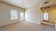 This single-floor residence offers a clean, functional layout designed for comfortable everyday living. The spacious living area is finished with plush wall-to-wall carpeting and neutral beige walls that create a bright, welcoming atmosphere. A sliding glass door and an adjacent window invite generous natural light while providing outdoor access. Track lighting overhead adds to the well-lit feel of the space. The kitchen is thoughtfully designed with dark wood cabinetry, a tile backsplash, black appliances including a refrigerator and range, and a peninsula breakfast bar with a granite-style countertop and integrated sink — ideal for casual dining or meal prep. A hallway connects the living spaces to the private areas of the home. The bedrooms are generously sized, each featuring soft carpeting, ceiling fans, and windows with horizontal blinds that offer both light control and privacy. One bedroom includes convenient closet access and an en-suite bathroom. The bathroom is outfitted with a full tub-and-shower combo featuring white tile surround, chrome fixtures, and hardwood-style flooring, lending a clean and classic finish. Throughout, the consistent use of warm neutral tones and carpet flooring contributes to a cohesive and comfortable living environment.