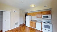 Located at 1030 N College in Indianapolis, Indiana, this single-floor space offers a practical and well-organized layout. The kitchen is a standout feature, equipped with warm honey-toned oak cabinetry that provides ample storage space. A full suite of white appliances is included, featuring a full-size refrigerator, electric range, built-in microwave, and dishwasher. The countertops offer a stone-like finish, providing a durable and functional workspace. Rich hardwood flooring flows throughout the space, adding warmth and a classic aesthetic to the interior. The neutral, light-toned walls create a bright and open atmosphere, complementing the natural tones of the cabinetry and flooring. The space is equipped with ceiling-mounted lighting and benefits from a wall-mounted HVAC system, ensuring year-round comfort. The open layout between the kitchen and the adjoining living area enhances the sense of spaciousness, making the space feel inviting and easy to navigate. Overall, the unit presents a clean, functional, and comfortable living environment well-suited for everyday living in Indianapolis.