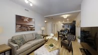Located at 50 Bridge St in Shelton, Connecticut, this one-bedroom, one-bathroom residence offers a well-designed, single-floor layout that maximizes comfort and functionality. The open-concept living area is anchored by warm hardwood-style flooring that flows seamlessly throughout the space, creating a cohesive and inviting atmosphere. The living room offers generous space for relaxing and entertaining, with clean white walls, recessed lighting, and ample room for furnishings. It opens directly into the dining area, which is bathed in warm light from a pendant fixture overhead, making it an ideal spot for everyday meals or hosting guests. The kitchen is thoughtfully appointed with dark cabinetry, stainless steel appliances including a microwave and range, and a refrigerator, providing both style and practicality. Track lighting illuminates the kitchen workspace efficiently. A hallway leads to the private bedroom and bathroom, offering a comfortable sense of separation from the main living areas. Throughout the residence, the neutral color palette, modern fixtures, and open sightlines contribute to a bright, airy ambiance that feels both contemporary and welcoming.