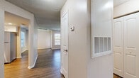 This single-floor residence offers a well-organized layout designed for comfortable living. The entryway welcomes visitors with rich, dark hardwood-style flooring that extends through the main living areas, complemented by neutral-toned walls and textured ceilings throughout. A hallway leads from the entry into the heart of the home, featuring a thermostat and wall-mounted HVAC vent for convenient climate control.

The living room is a standout space, anchored by a classic white brick fireplace and framed by a large window that invites abundant natural light. Track lighting adds a modern touch to the ceiling. The open layout connects seamlessly to adjacent areas, making the space feel expansive and cohesive.

The kitchen has been thoughtfully updated with crisp white shaker-style cabinetry, granite-look countertops, and a full suite of stainless steel appliances, including a refrigerator, dishwasher, and range. A corner sink beneath a window provides a pleasant view while preparing meals, and light wood-tone flooring ties the space together.

The bedrooms feature plush carpeting and windows overlooking the outdoors, creating a warm and restful atmosphere. The bathroom is finished with a white vanity, granite-style countertop, and a tiled shower-tub combination, reflecting the same clean aesthetic found throughout the home.