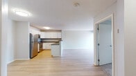 This single-floor residence offers a thoughtfully designed open-concept layout that seamlessly connects the kitchen and living areas. The kitchen is well-equipped with white shaker-style cabinetry, granite countertops, stainless steel appliances including a refrigerator, electric range, and built-in microwave, along with a peninsula that provides additional counter space and separation from the main living area. Light hardwood flooring runs throughout the main living spaces, lending warmth and visual continuity to the interior. The living area is generously proportioned and benefits from a sliding glass door that opens to a private balcony, inviting natural light and outdoor views into the space. The bedroom features plush carpeting, a large window with blinds, and access to a walk-in closet outfitted with a full-width hanging rod and shelving for practical storage. The bathroom is finished with a wide vanity featuring white cabinetry, a large mirror with overhead lighting, and a clean, neutral color palette. Throughout, the space maintains a consistent aesthetic of light tones and clean lines, creating a bright, modern, and comfortable living environment.