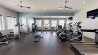 Located at 3258 Turtle Point Dr in Fayetteville, NC, this single-floor fitness center is a comprehensive workout facility designed to accommodate a wide range of exercise routines. The space is divided into distinct functional zones, each thoughtfully outfitted to support different training needs.

The cardio area is lined with multiple treadmills, elliptical machines, and stationary bikes, all positioned near large windows that allow natural light to fill the room and provide views of the surrounding greenery. Wall-mounted flat-screen televisions are positioned throughout the space for entertainment during workouts, and a wall clock keeps exercisers on schedule, complemented by posted 30-minute usage reminders for peak-hour courtesy.

The strength training section features a full rack of dumbbells displayed along a mirrored wall, offering excellent visual feedback during lifts. Several cable and resistance machines are strategically arranged throughout, providing options for targeting various muscle groups. Adjustable workout benches further add versatility to the free weight area.

The facility features durable rubber flooring throughout, ceiling fans for ventilation and comfort, and recessed lighting that maintains a clean, modern aesthetic. The walls are painted in a calming combination of white and soft teal-blue accents, contributing to an energizing yet focused atmosphere. Sanitization stations and posted facility rules reflect a commitment to cleanliness and user consideration.