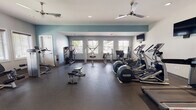 Located at 3258 Turtle Point Dr in Fayetteville, NC, this single-floor fitness center is a comprehensive workout facility designed to accommodate a wide range of exercise routines. The space is divided into distinct functional zones, each thoughtfully outfitted to support different training needs.

The cardio area is lined with multiple treadmills, elliptical machines, and stationary bikes, all positioned near large windows that allow natural light to fill the room and provide views of the surrounding greenery. Wall-mounted flat-screen televisions are positioned throughout the space for entertainment during workouts, and a wall clock keeps exercisers on schedule, complemented by posted 30-minute usage reminders for peak-hour courtesy.

The strength training section features a full rack of dumbbells displayed along a mirrored wall, offering excellent visual feedback during lifts. Several cable and resistance machines are strategically arranged throughout, providing options for targeting various muscle groups. Adjustable workout benches further add versatility to the free weight area.

The facility features durable rubber flooring throughout, ceiling fans for ventilation and comfort, and recessed lighting that maintains a clean, modern aesthetic. The walls are painted in a calming combination of white and soft teal-blue accents, contributing to an energizing yet focused atmosphere. Sanitization stations and posted facility rules reflect a commitment to cleanliness and user consideration.