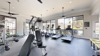 Located at 50 Estuary Trail in Alpharetta, Georgia, this fitness center is designed to provide a comprehensive and comfortable workout environment. The space is defined by floor-to-ceiling windows along multiple walls, flooding the interior with abundant natural light and offering views of the surrounding outdoor pool area and lush landscaping.

The facility is outfitted with a wide variety of cardio equipment, including multiple treadmills and elliptical trainers, each equipped with individual monitors for entertainment during workouts. A rowing machine further extends the cardio options available. For strength training, the center features cable machines, a multi-function cable tower, weight benches, and a selection of free weights including dumbbells and kettlebells. Stability and exercise balls add versatility for functional fitness routines.

Large wall-mounted mirrors enhance the sense of space and allow users to monitor their form throughout their workouts. Ceiling fans suspended from the well-appointed ceiling contribute to a comfortable, climate-controlled atmosphere. The durable rubberized flooring throughout the space is both practical and easy to maintain.

A wall-mounted flat-screen television provides additional entertainment options, and recessed lighting supplements the natural light for evening use. The overall aesthetic is clean, modern, and functional, creating an inviting environment well-suited for a full range of fitness activities.