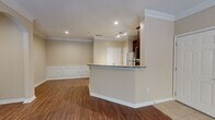 This single-floor, 2-bedroom, 1-bathroom residence offers a thoughtfully designed layout with refined finishes throughout. The open-concept living, dining, and kitchen area serves as the heart of the home, anchored by rich hardwood-style flooring and elegant crown molding. The kitchen is a standout feature, equipped with dark cherry wood cabinetry, granite countertops, stainless steel appliances, a tile backsplash, and a peninsula that provides both additional prep space and a natural divide from the living area. The living room is highlighted by a tray ceiling with a ceiling fan, access to the outdoors through a glass door, and ample natural light from large windows. Classic wainscoting panels add architectural charm to the dining and living areas. Both bedrooms are generously sized and bright, each featuring hardwood-style flooring, large windows with outdoor greenery views, and ceiling fans for comfort. The bathroom includes a full tub-shower combo finished with white tile and a decorative black diamond tile border accent. The entryway opens onto tile flooring that transitions seamlessly into the main living space, creating a cohesive and welcoming flow throughout the home.