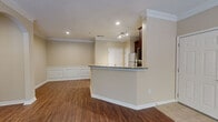 This single-floor, 2-bedroom, 1-bathroom residence offers a thoughtfully designed layout with refined finishes throughout. The open-concept living, dining, and kitchen area serves as the heart of the home, anchored by rich hardwood-style flooring and elegant crown molding. The kitchen is a standout feature, equipped with dark cherry wood cabinetry, granite countertops, stainless steel appliances, a tile backsplash, and a peninsula that provides both additional prep space and a natural divide from the living area. The living room is highlighted by a tray ceiling with a ceiling fan, access to the outdoors through a glass door, and ample natural light from large windows. Classic wainscoting panels add architectural charm to the dining and living areas. Both bedrooms are generously sized and bright, each featuring hardwood-style flooring, large windows with outdoor greenery views, and ceiling fans for comfort. The bathroom includes a full tub-shower combo finished with white tile and a decorative black diamond tile border accent. The entryway opens onto tile flooring that transitions seamlessly into the main living space, creating a cohesive and welcoming flow throughout the home.