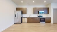 This two-story residence in Bluffdale, Utah offers a well-organized layout across two levels. The main living floor hosts the expansive open-concept kitchen and living room, where light hardwood flooring flows throughout. The kitchen is outfitted with warm wood-tone cabinetry, a white quartz countertop, a stainless steel undermount sink with a pull-down faucet, and a full suite of stainless steel appliances including a refrigerator with ice maker, dishwasher, microwave, and range. Recessed lighting illuminates both the kitchen and the generous living area, which features multiple windows that bring in natural light and views of the surrounding neighborhood. A hallway connects the living space to two well-proportioned bedrooms, each finished with plush carpeting and additional windows. The spacious primary bedroom includes an en-suite bathroom with a tub/shower combination, a wood-tone vanity, and light hardwood flooring. A second full bathroom mirrors this clean, contemporary aesthetic. The unit also includes a dedicated laundry area, a utility room, a closet, and carpeted staircases connecting the entry-level to the main floor, completing this thoughtfully designed home.