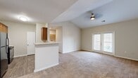 Located at 2350 Houston Lake Rd in Perry, Georgia, this single-story, three-bedroom, two-bathroom home offers a well-designed layout with comfortable living spaces throughout. The open-concept living and kitchen area is a defining feature, anchored by soaring vaulted ceilings and a ceiling fan that enhance the sense of spaciousness. A peninsula counter separates the kitchen from the living area, which flows naturally toward a set of French doors that invite natural light and outdoor access. The kitchen is well-appointed with warm wood cabinetry, light countertops, and black appliances including a range, refrigerator, and built-in microwave, all set on wood-look flooring. The living room is carpeted and bright, creating a welcoming gathering space. Three bedrooms provide comfortable retreats, each with plush carpeting, ceiling fans or lighting fixtures, and windows for natural light. The generously sized primary bedroom features vaulted ceilings and French doors. Two full bathrooms serve the home, one featuring a soaking tub with a tiled surround and curved shower rod. Two hallways connect the rooms efficiently, and a dedicated closet adds practical storage. The neutral color palette throughout gives the home a clean, move-in ready feel.