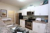 This single-floor residence offers a thoughtfully designed layout that balances comfort and functionality throughout its key living spaces. The kitchen is a standout feature, showcasing white cabinetry, granite-style countertops, stainless steel appliances, and a breakfast bar peninsula that opens to a dedicated dining area. A spacious walk-in pantry provides generous storage directly off the kitchen. The living room is warm and inviting, finished with plush carpet, a ceiling fan with light fixture, and a glass-panel door that opens to an outdoor area, allowing natural light to fill the space. A secondary sitting or flex room offers additional living space with neutral tones and soft carpet flooring. The primary bedroom is generously sized, featuring large windows with views to the outdoors, plush carpet, and direct access to a walk-in closet with wire shelving. A second bedroom mirrors the comfort of the primary, with ample natural light and a ceiling fan. Both bathrooms are cleanly finished, featuring granite-style vanity counters, white cabinetry, and tub-shower combinations with hardwood-style flooring. Throughout the residence, a cohesive neutral color palette and consistent finishes create a calm and welcoming ambiance.