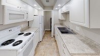 This single-floor residence offers a clean, functional layout designed for comfortable everyday living. The galley-style kitchen is well-equipped with white cabinetry, light stone-look countertops, a double-basin sink, recessed lighting, and white appliances including a refrigerator, electric range, and built-in microwave. Tile flooring runs throughout the kitchen, adding durability and easy maintenance to the space.

The living area features soft wall-to-wall carpeting and neutral gray walls, creating a welcoming atmosphere. A closeted entryway and an open passage to adjacent rooms contribute to the space's practical flow.

Multiple bedrooms are present, each finished with plush carpeting, neutral-toned walls, and individual windows dressed with blinds that allow for natural light while maintaining privacy. The rooms are generously sized and offer versatile layouts to suit a variety of needs.

The full bathroom is finished with tile flooring, white fixtures, and a tub and shower combination set against white square tile surround. Chrome hardware and a towel bar complete the clean, classic aesthetic.

Throughout the residence, consistent neutral tones, white trim, and carpeted flooring create a cohesive and move-in-ready environment that is both practical and comfortable.
