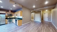 This single-floor residence offers a thoughtfully arranged layout with distinct living zones connected by a cohesive neutral color palette and light hardwood-style flooring that runs throughout the main areas. The open-concept kitchen and living space form the heart of the unit, where natural light maple cabinetry pairs with rich dark granite countertops to create a functional and visually appealing workspace. Stainless steel appliances, including a range, microwave, and refrigerator, complement the kitchen's clean aesthetic, while a built-in dishwasher adds everyday convenience. The adjacent living area is generously proportioned, offering a versatile open space illuminated by recessed lighting.

The bedroom areas are well-sized, with one room featuring plush carpeting and double closets with paneled white doors, providing ample storage. Additional rooms with hardwood-style flooring offer flexibility for various uses. The bathroom is equipped with a sleek walk-in shower enclosed by sliding glass doors and brushed nickel fixtures, set against a clean white surround. Throughout the unit, warm taupe walls, white baseboards, and recessed lighting contribute to a consistent, understated ambiance suited to a variety of interior styles.