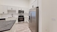 Located at 371 Technology Center Way in Rock Hill, SC, this modern single-floor residence showcases a bright, open layout with soaring ceilings and light-toned luxury vinyl plank flooring throughout. The open-concept kitchen is a standout feature, boasting crisp white shaker cabinetry, a classic subway tile backsplash, dark stone countertops, a large central island with pendant lighting, and a full suite of stainless steel appliances including a side-by-side refrigerator, electric range, and over-the-range microwave. The adjacent living area benefits from generous natural light through a sliding glass door that opens to an outdoor access point, complemented by a ceiling fan overhead. A secondary room features French doors that invite additional natural light, while additional bedrooms are well-proportioned with large windows and ample natural illumination. The primary bathroom is elegantly appointed with a dual-sink vanity topped with dark stone counters, an LED backlit mirror, wood-look flooring, and a subway-tiled walk-in shower. A soaking tub and a spacious walk-in closet with built-in shelving further enhance the primary suite. The overall aesthetic is clean, contemporary, and move-in ready.