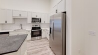 Located at 371 Technology Center Way in Rock Hill, SC, this modern single-floor residence showcases a bright, open layout with soaring ceilings and light-toned luxury vinyl plank flooring throughout. The open-concept kitchen is a standout feature, boasting crisp white shaker cabinetry, a classic subway tile backsplash, dark stone countertops, a large central island with pendant lighting, and a full suite of stainless steel appliances including a side-by-side refrigerator, electric range, and over-the-range microwave. The adjacent living area benefits from generous natural light through a sliding glass door that opens to an outdoor access point, complemented by a ceiling fan overhead. A secondary room features French doors that invite additional natural light, while additional bedrooms are well-proportioned with large windows and ample natural illumination. The primary bathroom is elegantly appointed with a dual-sink vanity topped with dark stone counters, an LED backlit mirror, wood-look flooring, and a subway-tiled walk-in shower. A soaking tub and a spacious walk-in closet with built-in shelving further enhance the primary suite. The overall aesthetic is clean, contemporary, and move-in ready.