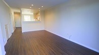 This two-floor residence offers a well-designed layout that balances functionality with a clean, modern aesthetic. The main living area is open and airy, featuring rich, dark hardwood-style flooring that runs throughout, creating a warm and inviting atmosphere. Recessed lighting in the ceiling provides even, ambient illumination across the space, complementing the neutral, light-toned walls that lend a bright and versatile canvas for any interior style.

A defining feature of the main level is the pass-through kitchen, which opens directly into the living area, promoting a connected and social atmosphere. The kitchen is outfitted with natural wood cabinetry that adds warmth and a classic character to the space. A window above the kitchen counter allows natural light to filter in, further brightening the interior.

Clean white baseboards frame the flooring throughout, adding a crisp, finished look to the overall design. The open floor plan of the living area provides generous room for flexible furniture arrangements, making it well-suited for both everyday living and entertaining. With two floors, the home offers ample room to accommodate distinct living and private spaces, making it a practical and comfortable residence overall.