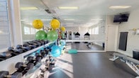 The Seasons EF 2 fitness center in Idaho is a thoughtfully designed, single-floor exercise facility built to support a well-rounded workout routine. The space features durable rubber flooring throughout, providing both safety and comfort underfoot during a variety of exercises. Large windows line the walls, flooding the room with abundant natural light and offering views of an outdoor pool area, creating an open and energizing atmosphere.

The facility is equipped with multiple cardio machines, including two treadmills and an elliptical trainer, positioned to take advantage of the natural light from the windows. A full wall-length mirror runs along one side of the room, visually expanding the space and allowing users to monitor their form during workouts. An adjustable weight bench and a rack of dumbbells in varying sizes offer comprehensive strength training options. Colorful stability balls in multiple sizes — green, yellow, and blue — along with step platforms, round out the functional training offerings.

A wall-mounted television is positioned for easy viewing across the exercise area, and posted workout guides offer exercise reference charts for users. The room is finished with clean white walls and bright overhead lighting, contributing to a crisp, well-maintained environment. Overall, the fitness center provides a practical, fully outfitted space for residents to pursue their health and wellness goals.