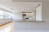Located at 74 Curlew Dr in Toronto's M3A neighbourhood, this single-floor, 2-bedroom, 2-bathroom residence offers a thoughtfully designed layout with a clean, modern aesthetic. The open kitchen is a standout feature, equipped with sleek white cabinetry, taupe countertops, large-format tile flooring, stainless steel appliances including a built-in oven, microwave, and refrigerator, and recessed pot lighting overhead. The kitchen flows seamlessly toward the living room, which is bathed in natural light from a wide bank of windows offering lush, tree-lined views. Warm hardwood flooring extends throughout the living areas and bedrooms, creating a cohesive and inviting atmosphere. The spacious primary bedroom includes mirrored sliding closet doors that enhance the sense of openness. The second bedroom also benefits from a large window with greenery views and gleaming hardwood floors. Both bathrooms are finished in a contemporary style — one features large grey wall tiles, a soaker tub with an overhead rain shower, chrome fixtures, and a vanity with integrated sink. The second bathroom is clean and minimalist in design. Soft grey tones on the walls throughout the unit create a calm, neutral palette ideal for modern living.