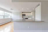 Located at 74 Curlew Dr in Toronto's M3A neighbourhood, this single-floor, 2-bedroom, 2-bathroom residence offers a thoughtfully designed layout with a clean, modern aesthetic. The open kitchen is a standout feature, equipped with sleek white cabinetry, taupe countertops, large-format tile flooring, stainless steel appliances including a built-in oven, microwave, and refrigerator, and recessed pot lighting overhead. The kitchen flows seamlessly toward the living room, which is bathed in natural light from a wide bank of windows offering lush, tree-lined views. Warm hardwood flooring extends throughout the living areas and bedrooms, creating a cohesive and inviting atmosphere. The spacious primary bedroom includes mirrored sliding closet doors that enhance the sense of openness. The second bedroom also benefits from a large window with greenery views and gleaming hardwood floors. Both bathrooms are finished in a contemporary style — one features large grey wall tiles, a soaker tub with an overhead rain shower, chrome fixtures, and a vanity with integrated sink. The second bathroom is clean and minimalist in design. Soft grey tones on the walls throughout the unit create a calm, neutral palette ideal for modern living.