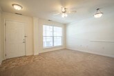 Located at 1056 Centerbrooke Lane in Suffolk, Virginia, this single-floor residence offers a clean, functional layout designed for comfortable everyday living. The open living area is finished with warm neutral carpet and crisp white walls accented by crown molding, creating a bright and welcoming atmosphere. A ceiling fan with a light kit provides both comfort and illumination, while a large window allows natural light to fill the space and offers views of the surrounding exterior. The living area flows seamlessly into a pass-through kitchen, which features light wood cabinetry, dark marbled laminate countertops, a stainless steel sink, and white appliances including a range and over-the-counter microwave. Stone-look tile flooring completes the kitchen's practical aesthetic. The bedroom is generously sized with plush carpeting, a ceiling fan, and the added convenience of two separate closets offering ample storage. The bathroom is finished with clean white fixtures, including a full soaking tub and shower combination with tiled surround, a safety grab bar, and stone-patterned tile flooring. Throughout the unit, the neutral palette and thoughtful design create a tidy, move-in-ready environment.