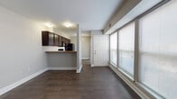 This single-floor unit in Charleston, South Carolina, presents a practical and cohesive layout designed for comfortable everyday living. The open living and dining area is finished with rich, dark hardwood-style flooring that extends throughout the main living spaces, complementing the neutral gray walls and crisp white baseboards. Large windows fitted with horizontal blinds allow natural light to fill the space, creating a bright and welcoming atmosphere.

The kitchen is accessible via a half-wall peninsula that provides both a casual dining surface and a visual separation from the living area. Dark espresso-toned cabinetry lines the walls from floor to ceiling, offering generous storage, while granite-style countertops add a refined touch. Black appliances, including a refrigerator, electric range, and over-the-range microwave, complete the kitchen's consistent aesthetic.

A hallway connects the main living area to the private quarters. The bedroom is carpeted for comfort and features two side-by-side closets with bifold doors, a ceiling fan with light fixture, and a window that brings in natural light. The bathroom is accessible from the bedroom area and includes a full tub-shower combination, toilet, and vanity with a granite-style countertop. A dedicated closet space adjacent to the bathroom provides additional storage.