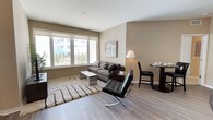This thoughtfully designed single-floor residence offers a harmonious blend of modern aesthetics and functional living. The open-concept living and dining area is anchored by large windows that flood the space with natural light and provide views of the surrounding outdoor landscape. Durable wood-style flooring runs throughout the main living areas, lending warmth and continuity to the overall design.

The kitchen is a functional centerpiece, featuring stainless steel appliances, a built-in microwave, ample cabinetry with under-cabinet lighting, and a generous peninsula with bar seating — ideal for casual dining or entertaining. White countertops and light-toned cabinetry keep the space feeling bright and clean.

The bedrooms are comfortably sized, each featuring plush carpeting and neutral wall tones that create a calm, restful atmosphere. One bedroom includes a walk-in closet offering generous storage, while the other provides easy access to closet space. Both bathrooms are finished with tile flooring, modern vanities with white countertops, and large mirrors that enhance the sense of space.

Throughout the residence, a consistent neutral color palette, clean lines, and contemporary finishes come together to create a cohesive and inviting living environment suited for everyday comfort.