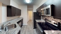 This single-floor residence offers a thoughtfully designed layout across several well-defined living spaces. The open living area is finished with warm neutral-toned walls, plush carpet, and elegant crown molding, with a fireplace serving as a notable architectural focal point. A pass-through opening connects the living space to the kitchen, which is outfitted with dark espresso cabinetry, granite-style countertops, a decorative tile backsplash, and a full suite of stainless steel appliances including a refrigerator, electric range, microwave, and dishwasher. Wood-look flooring runs throughout the kitchen, complementing its contemporary finishes.

The bedrooms are carpeted and bathed in natural light through large windows with blinds. The primary bedroom features a tray ceiling and direct access to a spacious walk-in closet with built-in shelving. Two full bathrooms serve the home; one includes a wide vanity with dual sinks and a large mirror, while the other offers a clean, white tub-shower combination, single vanity, and wood-look flooring. Throughout, the space maintains a consistent, neutral color palette that creates a cohesive and inviting atmosphere.