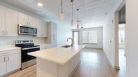 Located at Tomoka Town Center in Daytona Beach, FL, this well-appointed one-bedroom, one-bathroom unit offers a thoughtfully designed open-concept layout. The kitchen serves as a centerpiece, featuring a large island with a quartz countertop and an integrated sink with a gold-toned faucet, complemented by sleek gray cabinetry, stainless steel appliances — including a side-by-side refrigerator, electric range, and microwave — and elegant pendant lighting overhead. The kitchen flows seamlessly into the living area, which is bathed in natural light through large windows and a glass door, and is outfitted with a ceiling fan. Light wood-style flooring extends throughout the main living spaces, enhancing the bright, airy atmosphere. The spacious primary bedroom features a ceiling fan, large windows with blinds, and a sliding glass door that invites additional natural light. The dedicated closet includes multi-level wire shelving, offering generous storage. The bathroom is finished with large-format white tile flooring, a clean white vanity, and a full soaking tub with a tiled surround. A separate laundry room houses a full-size washer and dryer, adding everyday convenience to this modern Daytona Beach residence.