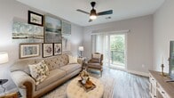 This thoughtfully designed 2-bedroom, 2-bathroom residence in Manchester, NH offers a cohesive blend of modern finishes and functional living across a single floor. Light gray wood-look flooring runs throughout, tying each space together seamlessly. The living room is a welcoming centerpiece, featuring a ceiling fan, large sliding glass doors that open to a private balcony with tree-lined views, and generous wall space ideal for displaying art. The kitchen is outfitted with white shaker cabinetry, white quartz countertops, subway tile backsplash, stainless steel appliances, and a peninsula with bar seating illuminated by pendant lighting — perfect for casual dining or entertaining. The spacious primary bedroom accommodates a full suite of furniture comfortably and is complemented by its own closet. The second bedroom offers equally practical proportions with natural window light. Both bathrooms are finished with white vanities, black hardware accents, and a tub-shower combination. One bathroom conveniently houses an in-unit washer and dryer. Three closets provide ample storage throughout the residence. The overall palette of soft grays and whites lends the space a clean, modern aesthetic.