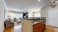 Located at 2155 Benton Blvd in Savannah, GA, this well-appointed 2-bedroom, 1-bathroom single-floor residence offers a thoughtfully designed layout across a compact yet efficient footprint. The open-concept kitchen and living area serves as the heart of the home, featuring warm honey-toned cabinetry, dark granite-style countertops, a double-basin sink, and black appliances including a range, microwave, and refrigerator. A peninsula counter connects the kitchen to the living space, which showcases beautiful hardwood flooring, crown molding, and large windows that flood the area with natural light. The living room provides a comfortable, airy atmosphere, complemented by a ceiling fan and ample wall space. An adjacent dining area accommodates a round table beneath an elegant chandelier, with a large window framing views of the outdoors. The primary bedroom features plush carpet, a ceiling fan, natural light through slatted blinds, and access to a generously sized walk-in closet with built-in shelving. The bathroom includes warm wood cabinetry, a wide vanity with a white countertop, a large mirror, and tile flooring. A connecting hallway ties all rooms together for a smooth, functional flow throughout the home.