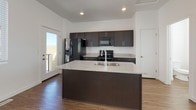 This two-story home is designed with a clean, modern aesthetic throughout. The main level centers on an open-concept living and kitchen area, where light wood-tone laminate flooring flows seamlessly across a generously sized floor plan. The kitchen is well-appointed with dark espresso cabinetry, granite-look countertops, and a suite of black appliances including a gas range, microwave, and a stainless side-by-side refrigerator. A large center island with a double sink and matching granite surface serves as both a functional workspace and a natural gathering point. Sliding glass doors and additional windows bring in natural light and provide access to an outdoor balcony area. A conveniently located half bathroom on the main level features a pedestal sink, toilet, and a window that brightens the space.

Upstairs, the bedrooms feature neutral carpet, white walls, and access to closet space. The full bathroom on this level includes a tub-shower combo, a dark-cabinet vanity with a granite countertop, and wood-look flooring. Throughout both floors, recessed lighting, white walls, and clean finishes contribute to a bright, contemporary atmosphere.
