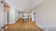 Located at 229 E Chatham St in the heart of downtown Cary, NC, this well-appointed 2-bedroom, 2-bathroom residence offers a thoughtfully designed single-level layout. The open-concept kitchen and living area serves as the centerpiece of the home, featuring white shaker cabinetry, a classic subway tile backsplash, stainless steel appliances, and a gray center island with a crisp white quartz countertop illuminated by modern glass pendant lights. The living area is bathed in natural light from a large bank of windows and includes a ceiling fan and direct access to an outdoor area. Light hardwood-style flooring flows throughout the main living spaces, enhancing the bright, airy ambiance. The primary bedroom offers comfortable proportions with plush carpeting, while its en-suite bathroom includes a white vanity with gold-toned fixtures, a tub-shower combo with tile surround, and a walk-in closet. The second bedroom is equally well-lit, with a large window and direct closet access to a shared full bathroom. Additional conveniences include in-unit laundry, a utility room, and a connecting hallway for seamless circulation. The neutral color palette and clean architectural lines give the space a fresh, modern character.