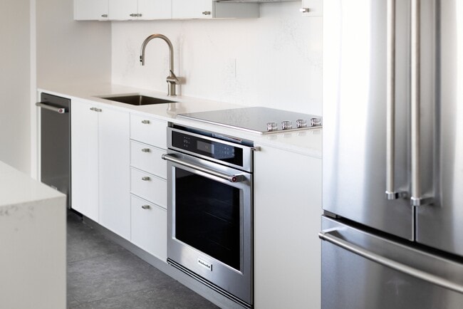 Signature Collection kitchen with white cabinetry, white marbled quartz countertop and backsplash, wine fridge, and upgraded stainless steel appliances - Avalon South Miami Apartments