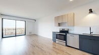 Located at 310 N Second St in Minneapolis's vibrant North Loop neighborhood, this contemporary one-bedroom, two-bathroom residence offers a thoughtfully designed single-floor layout with a clean, modern aesthetic throughout. Light-toned hardwood-style flooring flows seamlessly across every room, complementing the bright white walls and creating a cohesive, airy atmosphere.

The open-concept kitchen and living area serves as the heart of the home. The kitchen is outfitted with a full suite of stainless steel appliances—including a French door refrigerator, electric range, and dishwasher—paired with two-toned cabinetry featuring matte dark lower cabinets and natural wood upper cabinets. A vertical white tile backsplash and sleek countertops complete the modern look. The living area connects directly to a private balcony through a large floor-to-ceiling sliding glass door, inviting natural light and outdoor views.

The bedroom is a calm, well-proportioned retreat with clean white walls and ample floor space. It is served by a dedicated closet and easy access to the two bathrooms. A separate laundry room houses a stacked washer and dryer unit alongside built-in shelving, offering convenient in-unit functionality. Black matte hardware accents on interior doors add a sharp, contemporary finishing touch throughout the space.