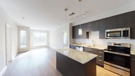 This single-floor residence showcases a contemporary design with high-quality finishes throughout. The kitchen is a standout feature, boasting dark espresso cabinetry that extends to the ceiling, a classic white subway tile backsplash, and light granite countertops on both the perimeter surfaces and a central island. Stainless steel appliances, including a refrigerator, range, microwave, and dishwasher, complete the well-appointed culinary space. Pendant lighting and a track rail system illuminate the kitchen and adjacent living area, which features warm hardwood flooring and large windows that invite generous natural light.

A carpeted bedroom with neutral tones opens through French doors to an outdoor area, providing a seamless indoor-outdoor connection. The bathrooms are finished with large-format tile flooring, floating dark-wood vanities, white countertops, and oversized mirrors. An in-unit stacked washer and dryer adds everyday convenience. A walk-in closet with wire shelving offers ample storage. The overall layout, visible through the 3D floor plan, presents a well-organized flow between living, sleeping, and utility spaces, all unified by a consistent modern aesthetic.